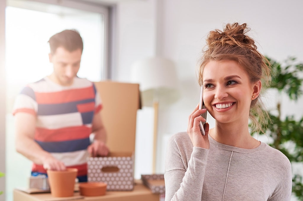 Eine Frau telefoniert am Handy während ein Mann Umzugsgut verpackt