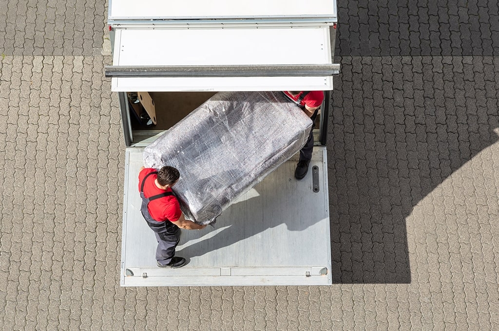 Zwei Umzugshelfer laden eine Couch aus einem LKW