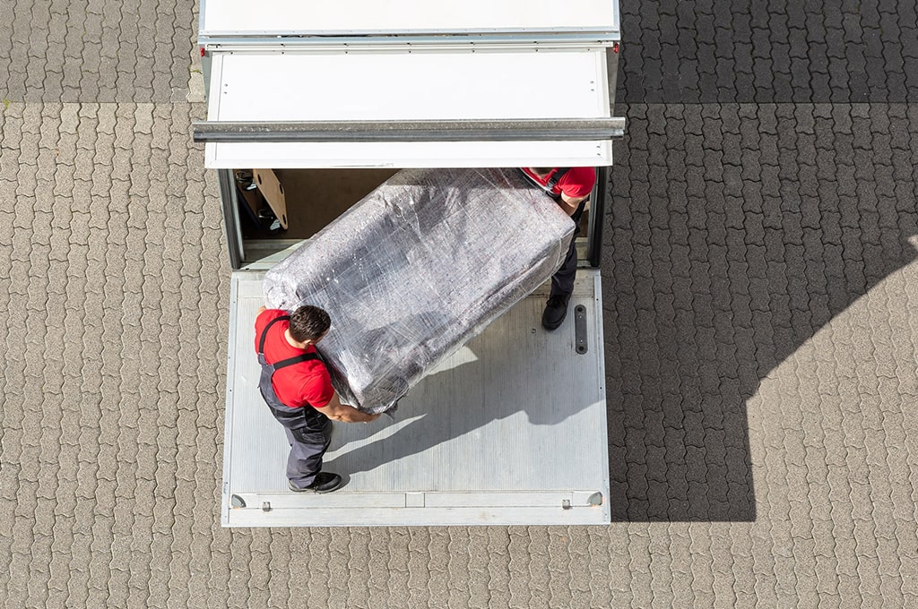 Zwei Umzugshelfer laden eine Couch aus einem LKW